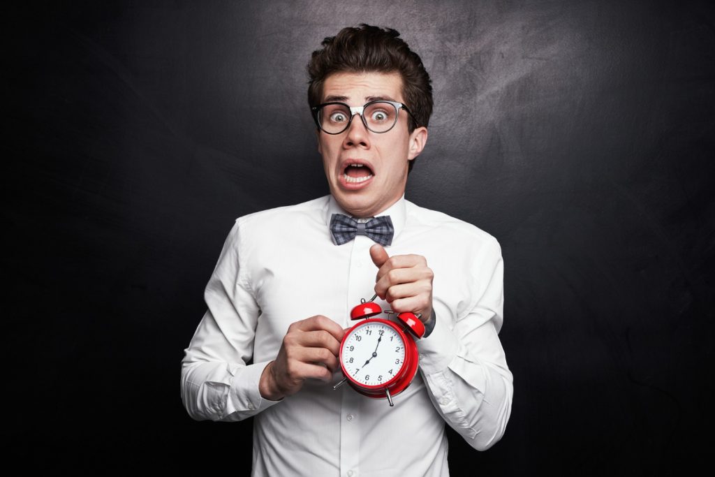 Young man in glasses is holding an alarm clock